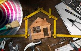 Wooden model house with folding ruler, work tools and a calculator on a wooden desk