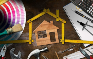 Wooden model house with folding ruler, work tools and a calculator on a wooden desk