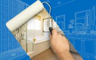 A digital composite image of a hand holding a paint roller and painting a bathroom. The left side shows a finished, modern bathroom with a tub, glass shower, and tile walls. The right side shows a blue background with a white line-art drawing of a bathroom with a double vanity and mirrors, as if it is a blueprint being painted over.