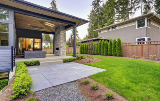 Modern residential outdoor patio cover extending from a house, featuring wood plank ceiling and a stone pillar, illustrating the maintenance needed for the covered deck and surrounding landscaping.